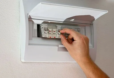 Ruka přepíná jistič v rozvaděči pro instalaci vodiče.