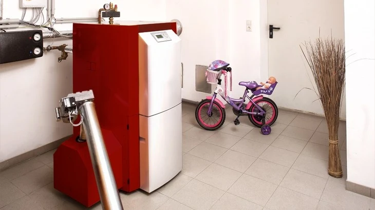Červený kotel vedle dětského bicyklu v technické místnosti.