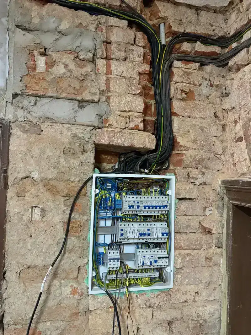 Otevřená rozvaděč s jističi a propojenými vodiči na cihlové zdi.