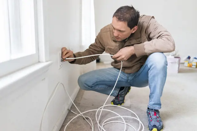 Muž instaluje elektrické vedení do zdi u okna.