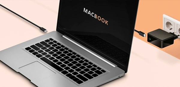 Otevřený MacBook s nabíječkou připojenou k elektrické zásuvce.