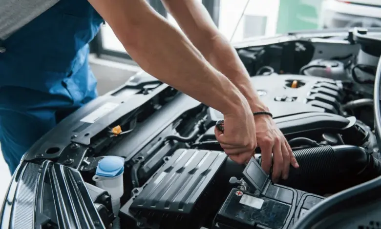 Mechanik opravuje automobilovou baterii pod kapotou.