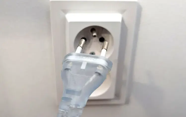 Prozrazný elektrický zástrčka v bílé zásuvce na stěně.
