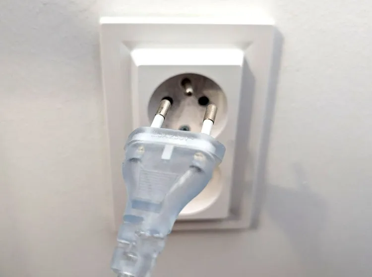 Prozrazný elektrický zástrčka v bílé zásuvce na stěně.