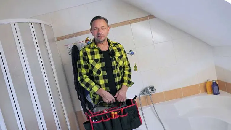 Muž s nářadím v koupelně připravuje na opravu sprchové baterie.