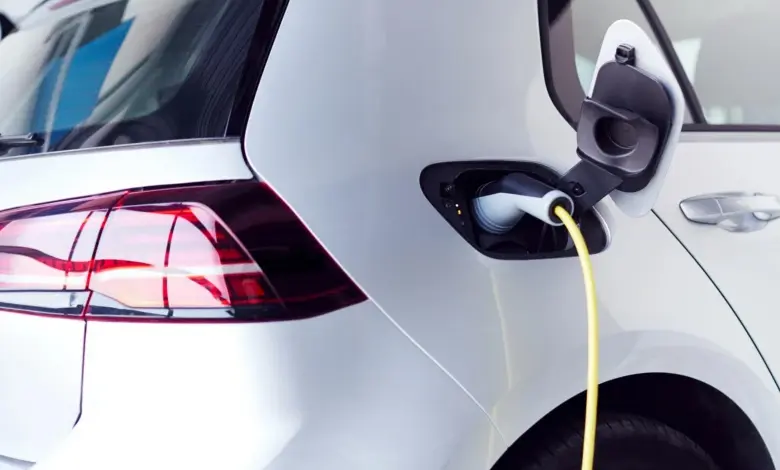 Bílý elektromobil nabíjen žlutým kabelem u zadního nárazníku.