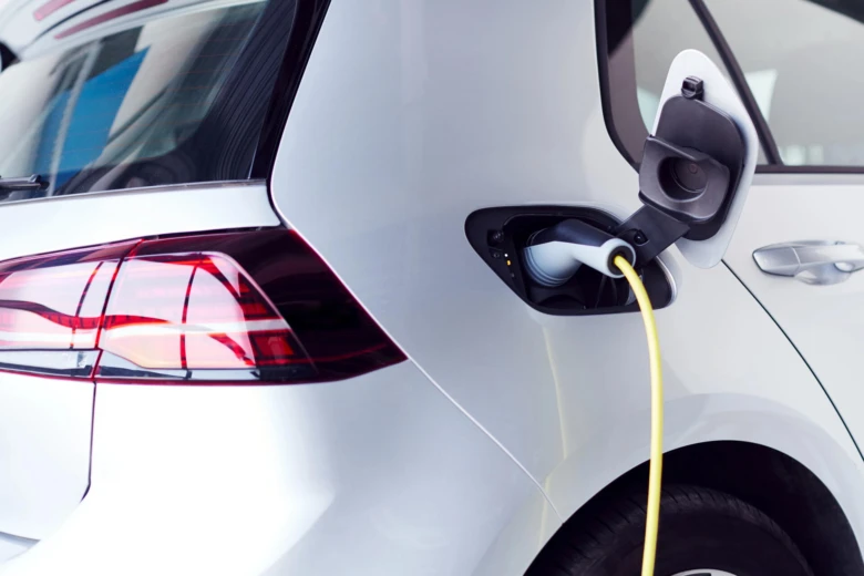 Bílý elektromobil nabíjen žlutým kabelem u zadního nárazníku.