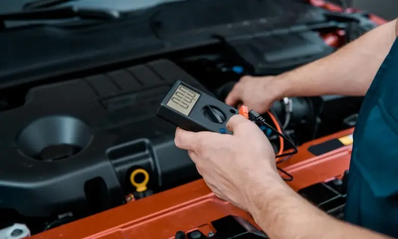 Mechanik měří napětí automobilové baterie multimetrem pod kapotou.