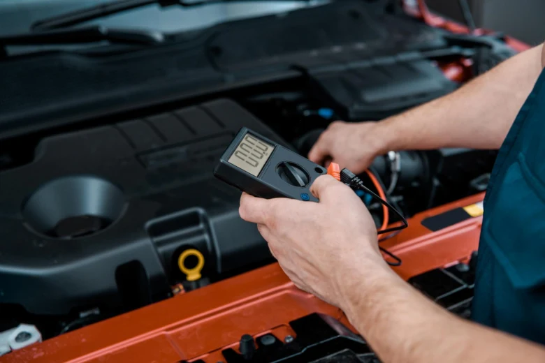 Mechanik měří napětí automobilové baterie multimetrem pod kapotou.
