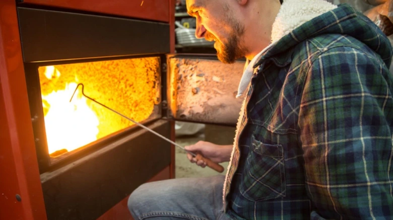 Muž upravuje hořící uhlí v topidle pro vytápění domu.