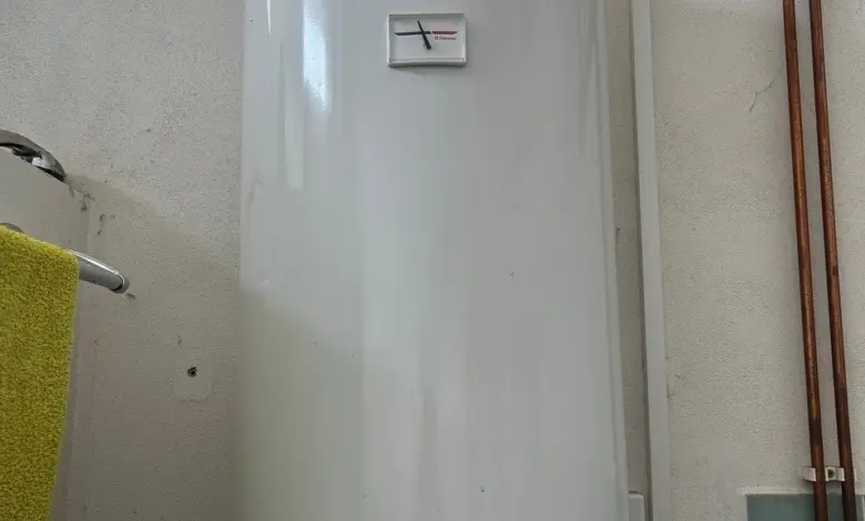 Bílý elektrický bojler na zdi s měřidlem teploty.