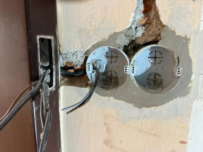 Odkryté elektrické vedení s dvěma zásuvkovými krabicemi v zdi panelového domu.