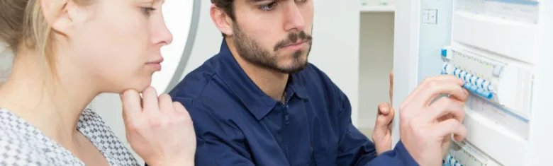 Elektrikář kontroluje jistič v rozvaděči s ženou.