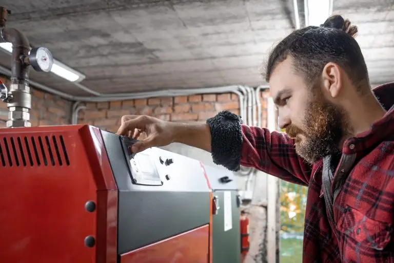 Muž nastavuje ovládací panel na červeném kotli na pelety.