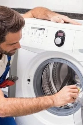 Montér zapojuje pračku do kanalizace pomocí hadice.