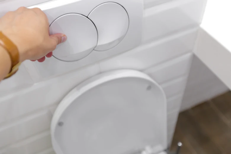 Ruka tlačí na splachovací tlačítko u bílého WC s dvojitým plněním.