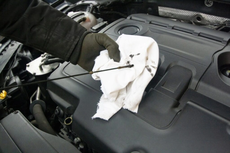 Ruka otírá olejovou tyč v motoru čistým hadříkem.