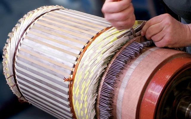 Technik opravuje vinutí v elektromotoru ručními nástroji.