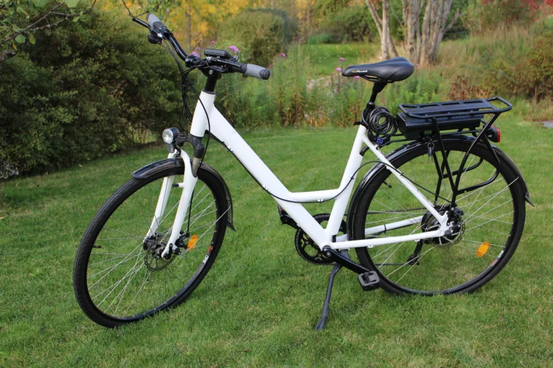 Bílý elektrobikl stojí na trávníku před keři.