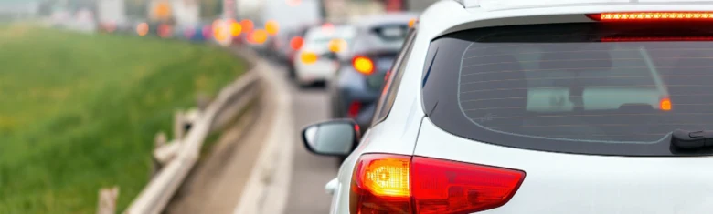 Bílý automobil s rozsvícenými zadními světly v provozu na silnici.