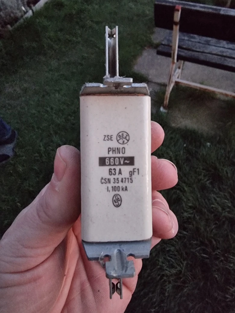 Ruka drží elektrický jistič v keramickém pouzdře venku.