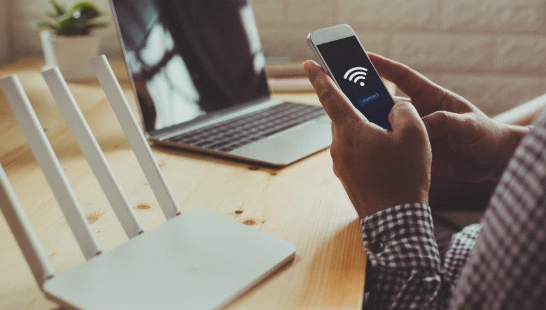 Osoba drží chytrý telefon u bezdrátového routera s anténami.