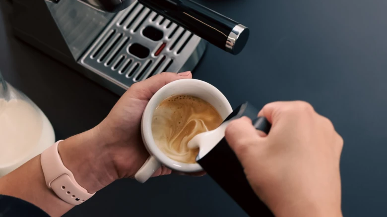 Lidé nalévají mléko do šálku s kávou pro cappuccino.