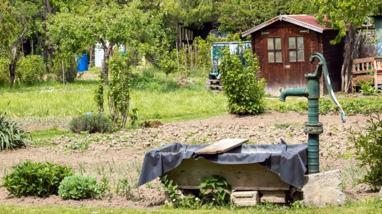 Zelená ruční čerpadlo ze studny s nádrží v zahradě.