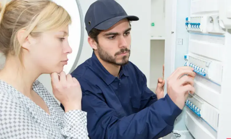 Elektrikář kontroluje jistič v rozvaděči s klientkou.