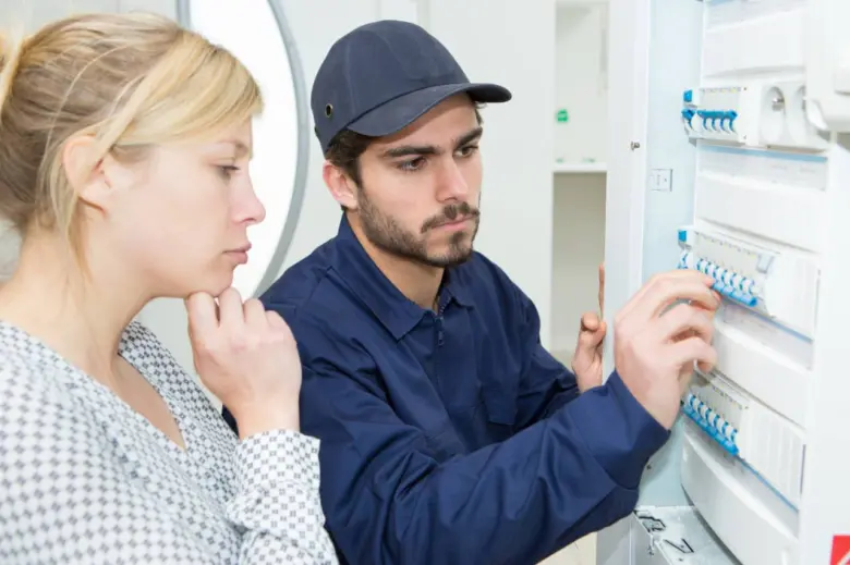 Elektrikář kontroluje jistič v rozvaděči s klientkou.