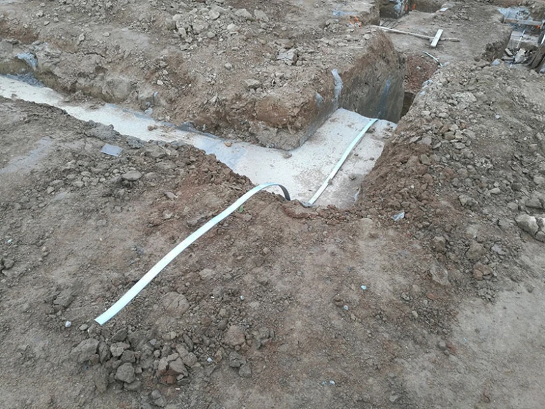 Bílý vodič uzemnění uložený v vykopaném příkopu pro elektroinstalaci.