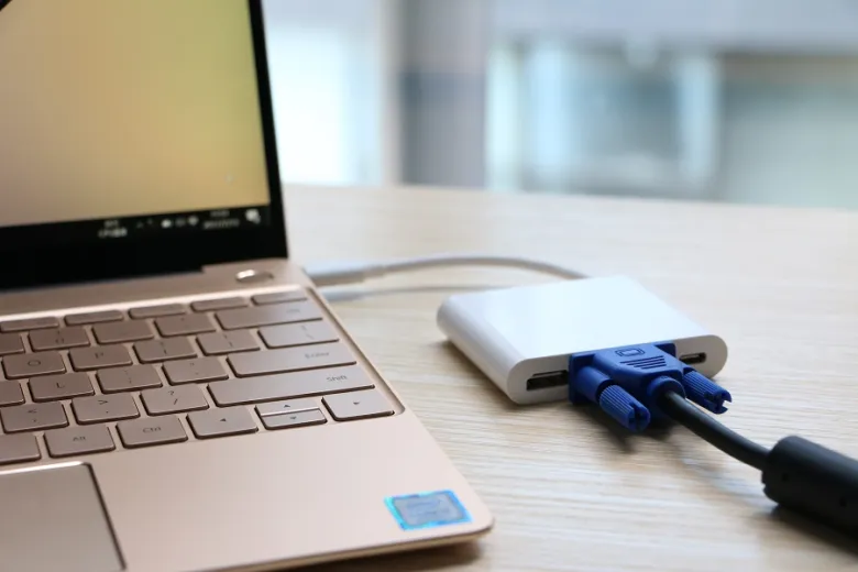 Zlatý notebook připojený přes adaptér HDMI k projektoru s modrými kabely.