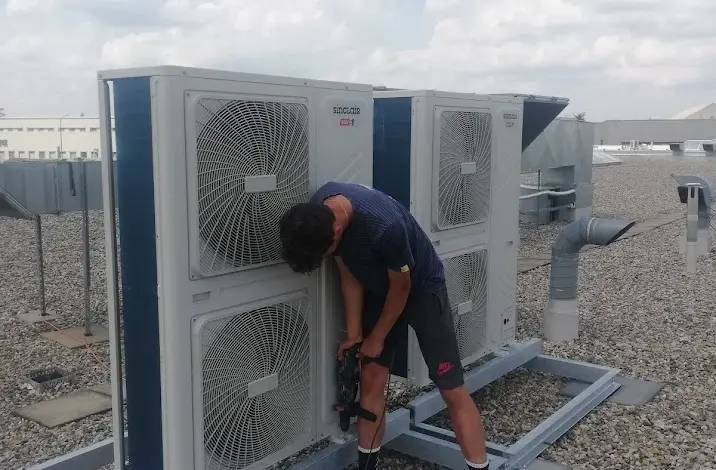 Technik opravuje venkovní jednotku klimatizace na střeše.