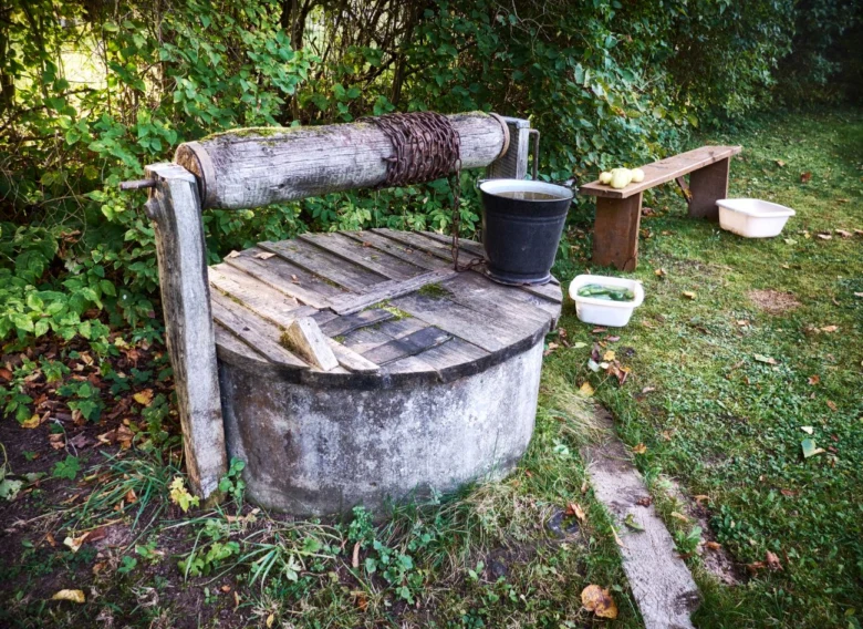 Stará dřevěná studnice s kbelíkem a lavičkou v zahradním prostředí.