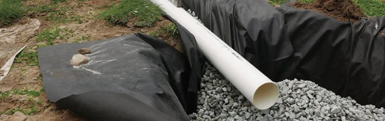Bílá odvodňovací trubka na štěrku pro správný odtok vody z okapu.