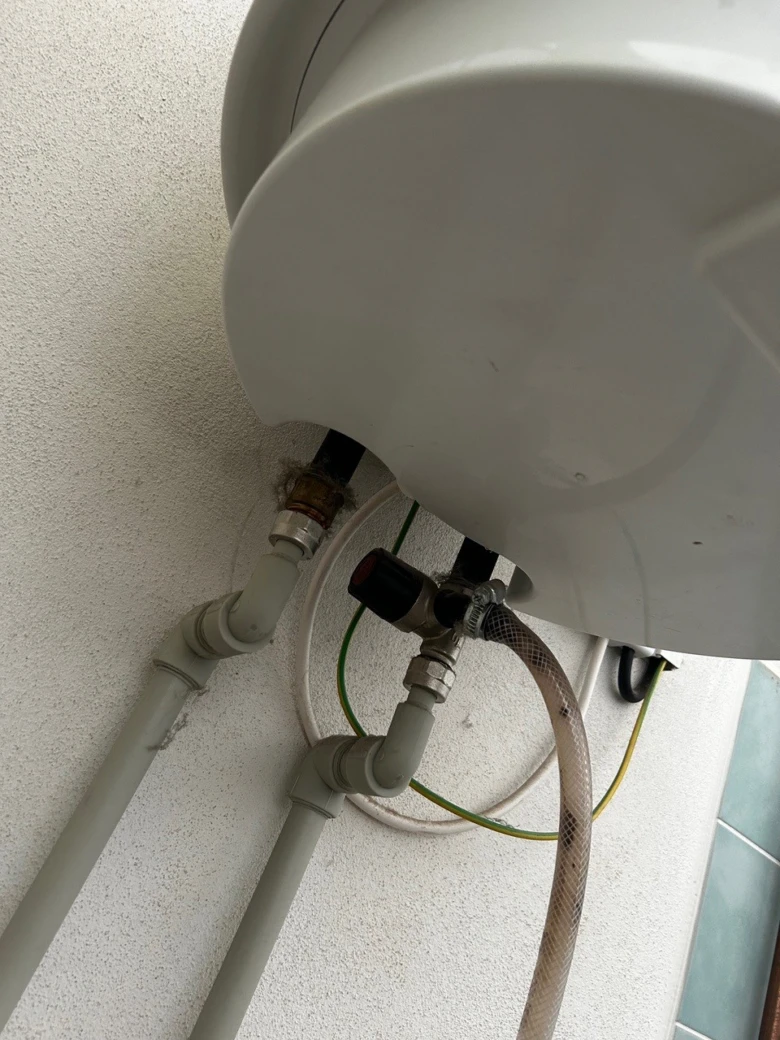 Elektrický bojler s připojenými vodovodními potrubími na zdi.