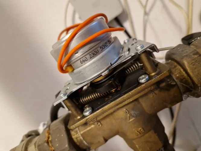 Blízký záběr na třístupňový ventil s elektromagnetickou cívkou a odšroubovaným krytem.