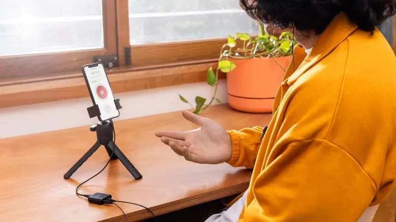 Osoba používá externí mikrofon připojený k telefonu na stativu pro videohovor.