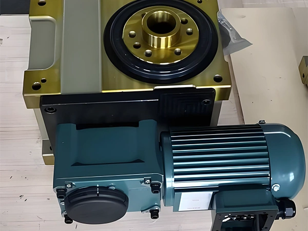 Třífázový elektromotor připojený k převodovce na dřevěné podlaze.