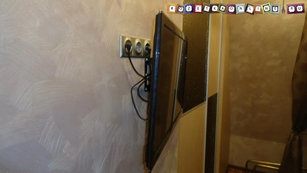 Televize namontovaná na stěně s elektrickými zásuvkami pro napájení.