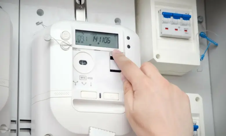 Ruka stiská tlačítko na chytrém elektroměru s displejem.