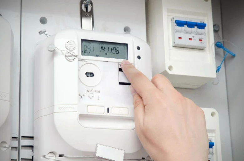 Ruka tlačí na displej chytrého elektroměru s časem a daty.