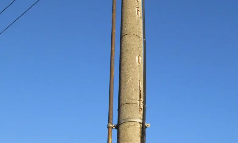 Konkrétní elektrický sloup s vedením na modré obloze.