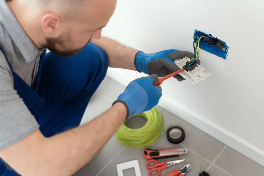 Elektrikář opravuje zásuvku na zdi s nástroji.