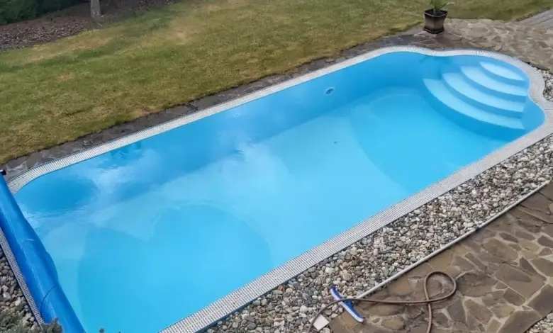 Prázdný bazén s částečně odvinutou krycí plachtou na zahradě.