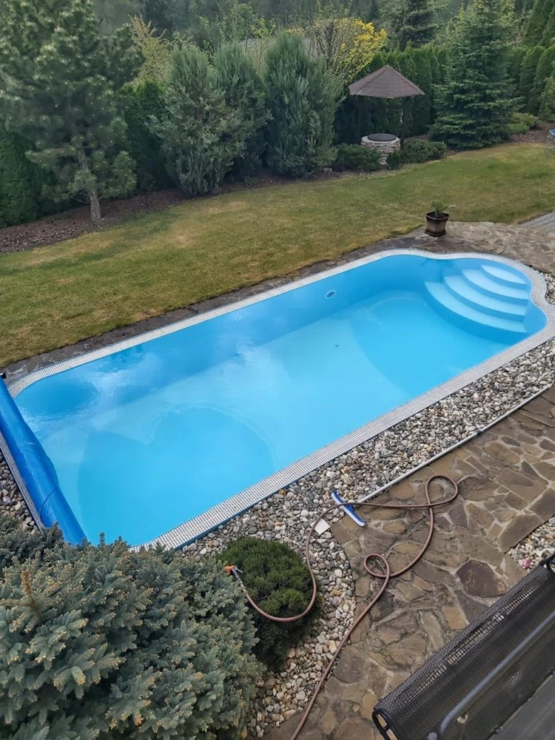 Prázdný bazén s částečně odvinutou krycí plachtou na zahradě.