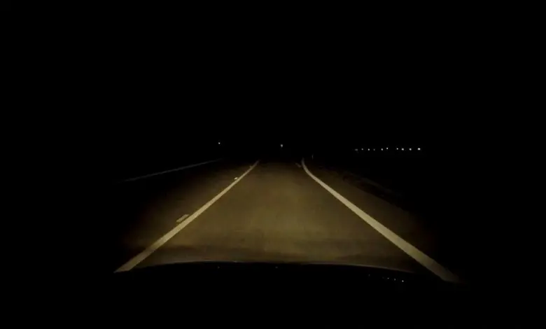 Autobusové světla osvětlují prázdnou silnici v noci.