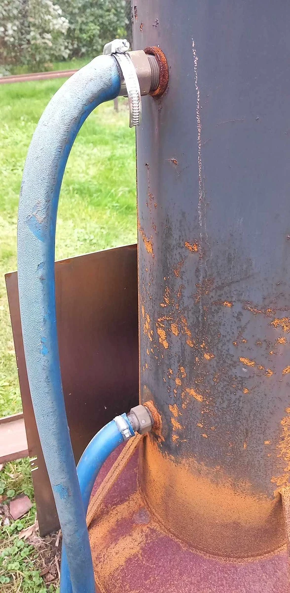 Modré hadice připojené k bazénovému ohřívači na dřevo venku.