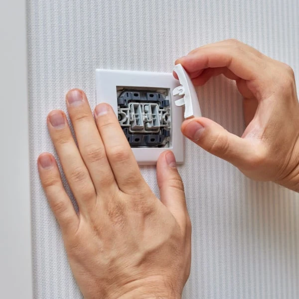 ruce montují bílý kryt na elektrický vypínač s viditelnými kontakty.