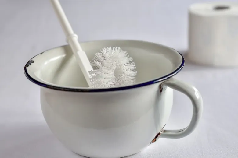 Bílá škrabka na záchod v hrnku s rolí toaletního papíru.